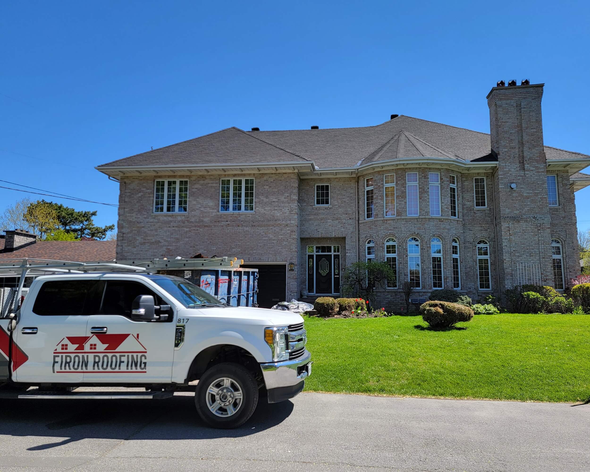 White pickup truck with a ladder on top parked on a street. The truck has Firon Roofing, a roofing company serving the Ottawa and Gatineau region, written on the door with a red house roof logo. Trees and a cloudy sky are visible in the background.