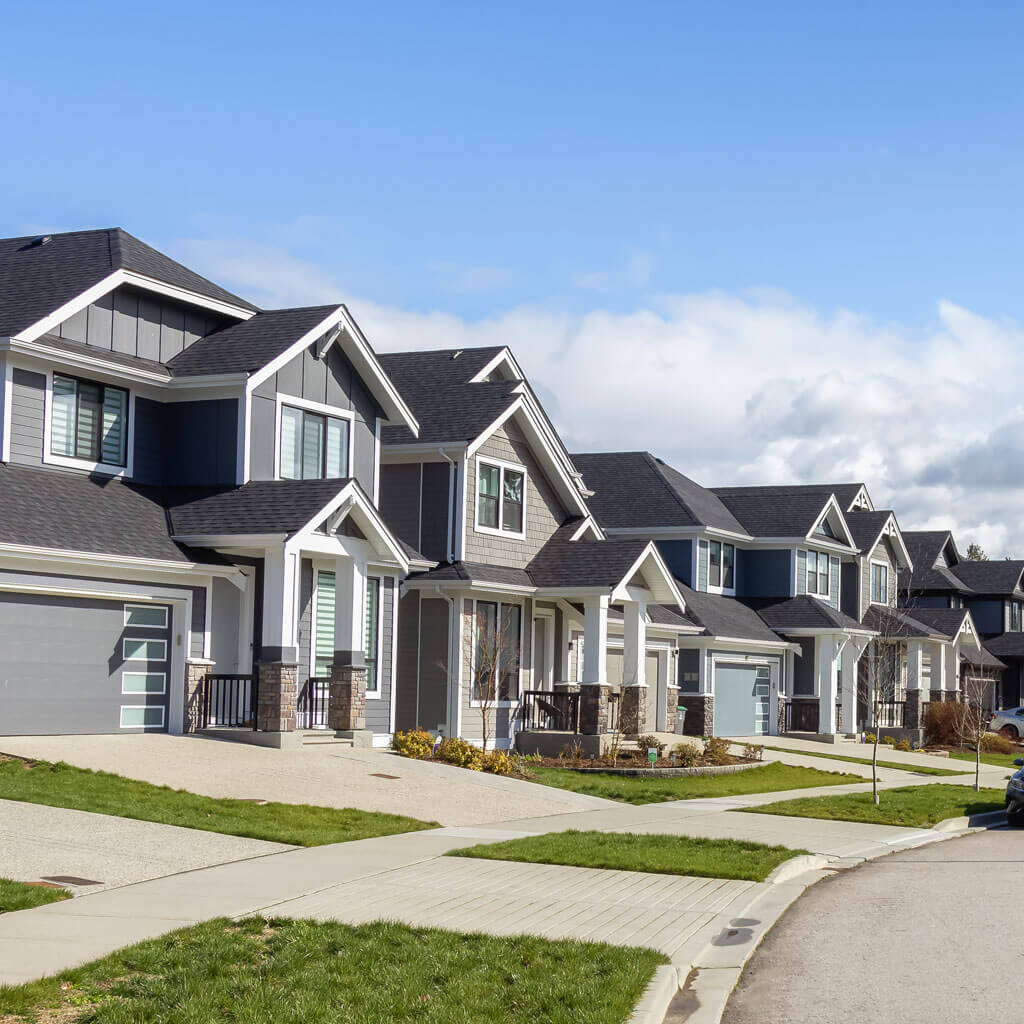 Une rangée de maisons modernes de banlieue à deux étages, avec un revêtement gris, de grandes fenêtres et des garages attenants, bordent une rue calme. Les pelouses et allées bien entretenues complètent chaque maison — des candidates idéales pour un ajustement de toiture fiable à Ottawa.
